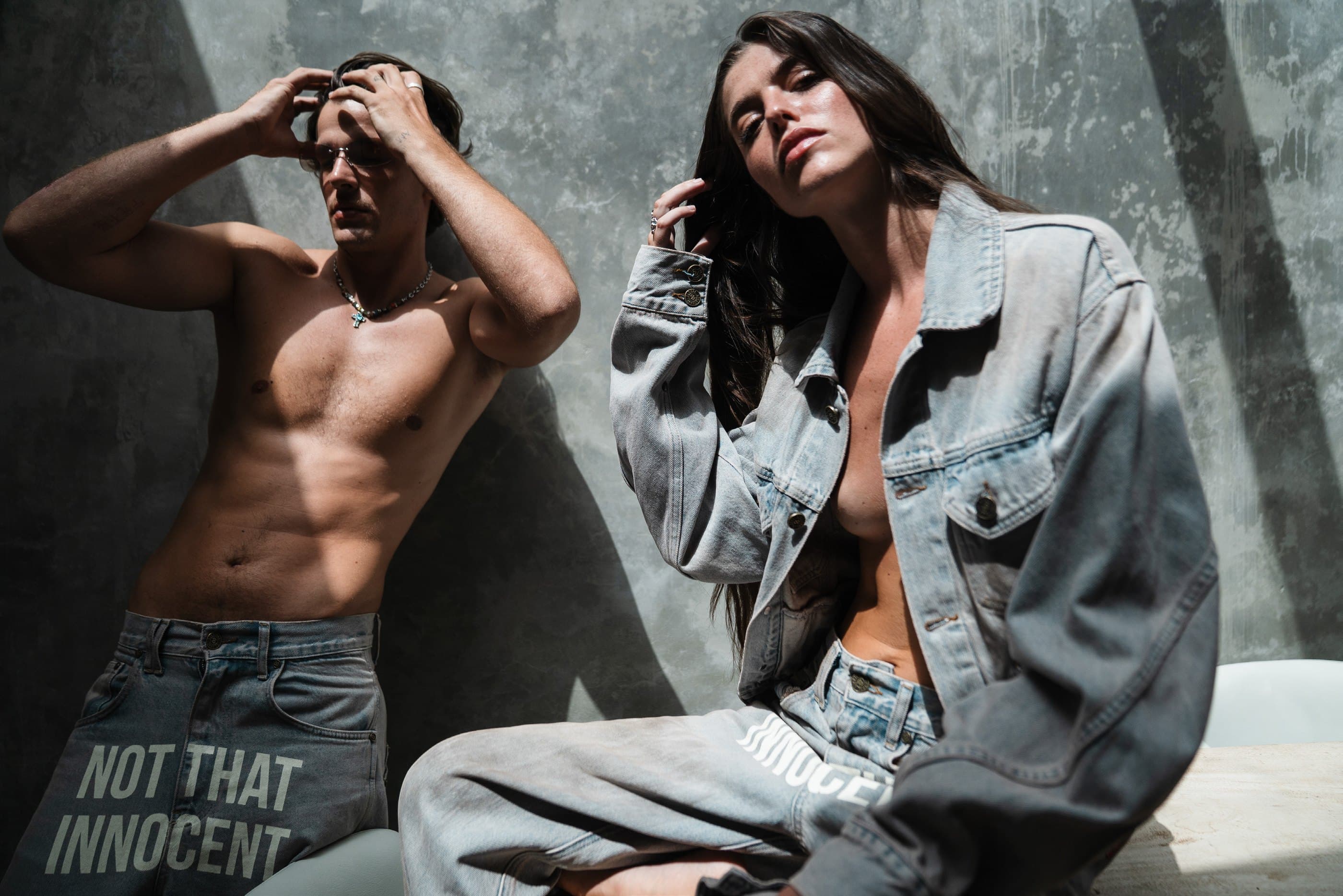 Two models in The Origin Jean and The Origin Jacket against a concrete wall.